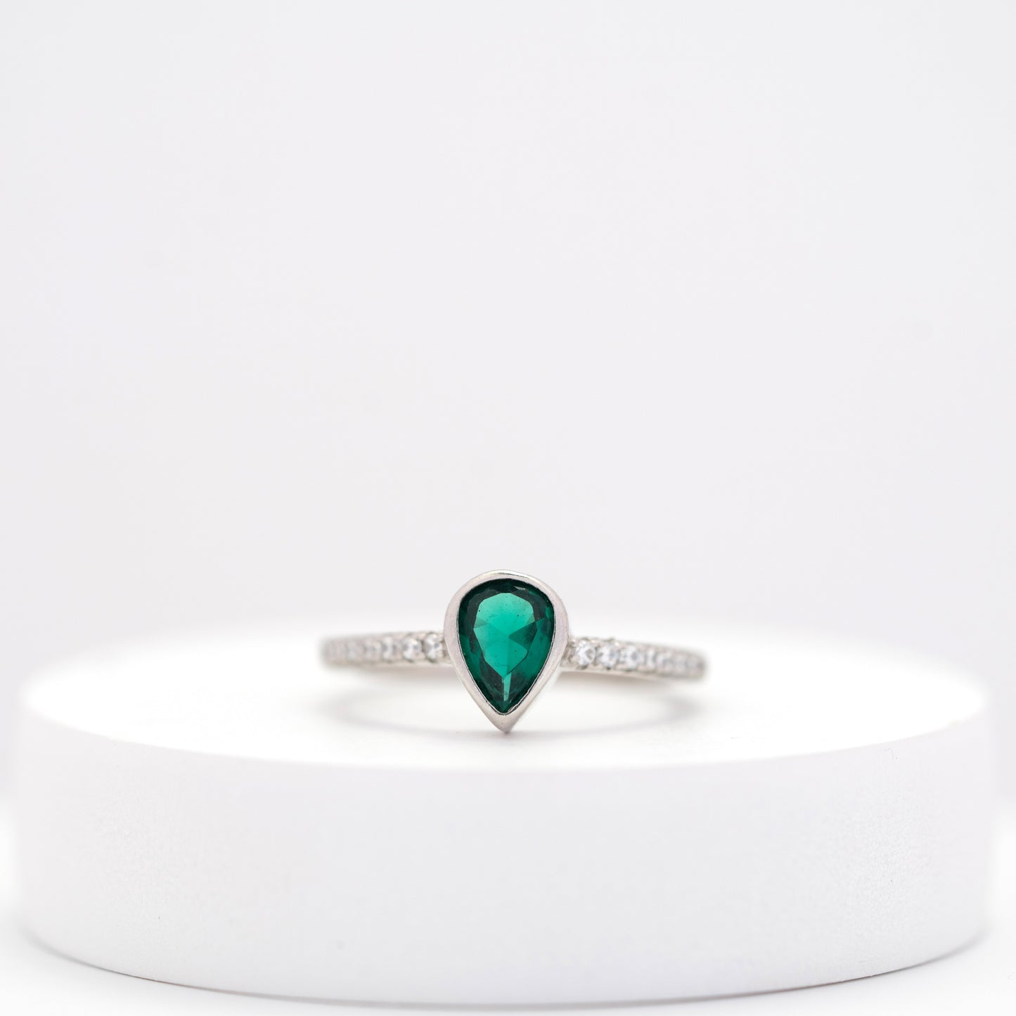 front view of elegant silver ring with teardrop emerald center stone and side diamonds