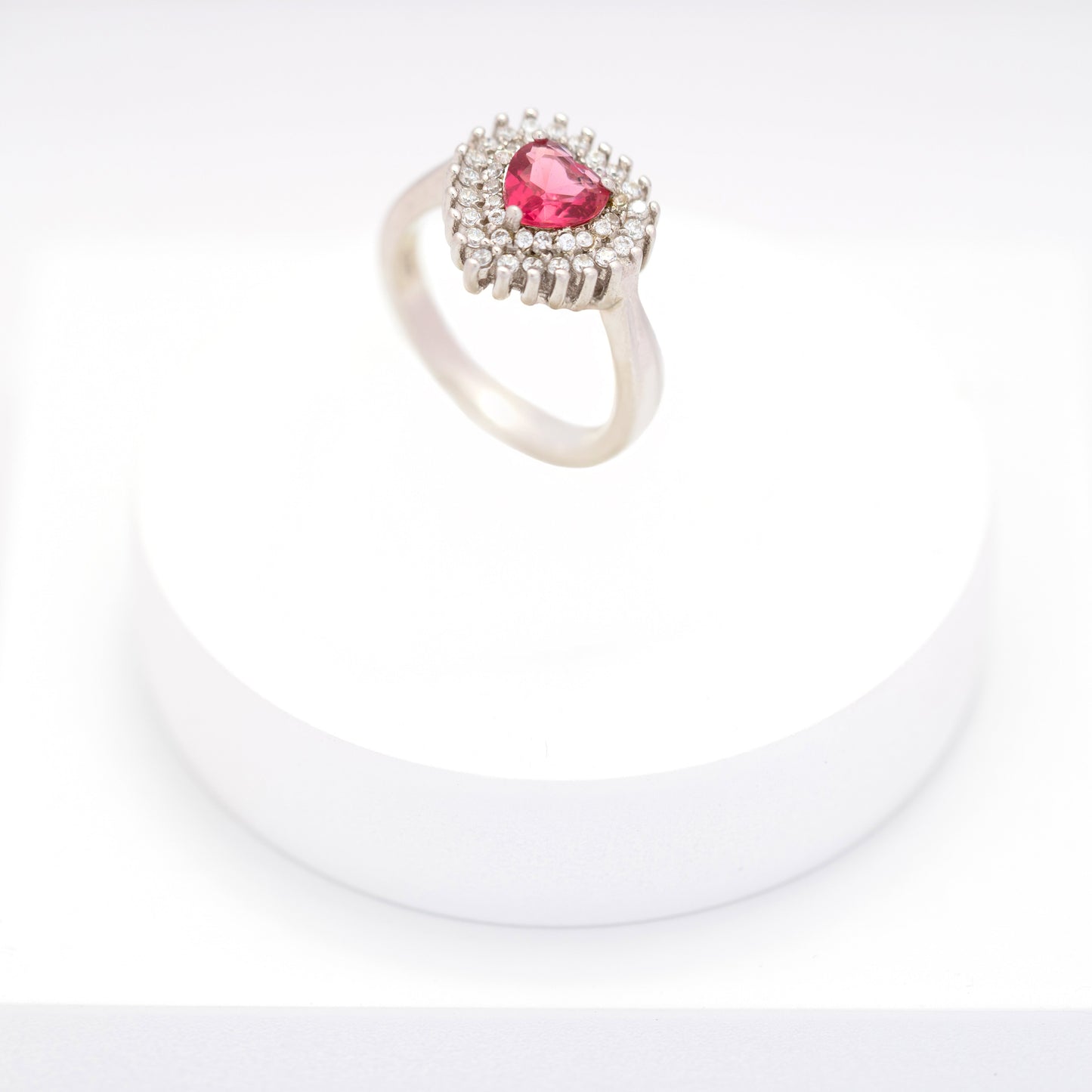 Silver ring with heart-shaped pink sapphire and diamond halo on a white stand