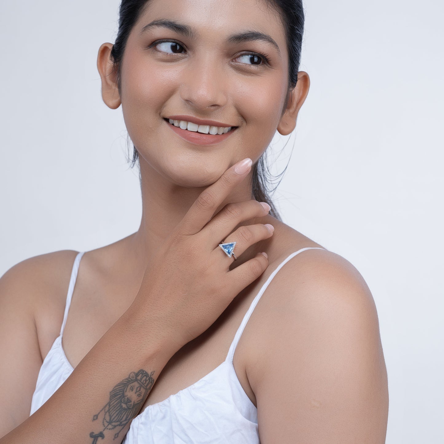Woman smiling and wearing a triangular blue gemstone ring on her finger, against a plain background