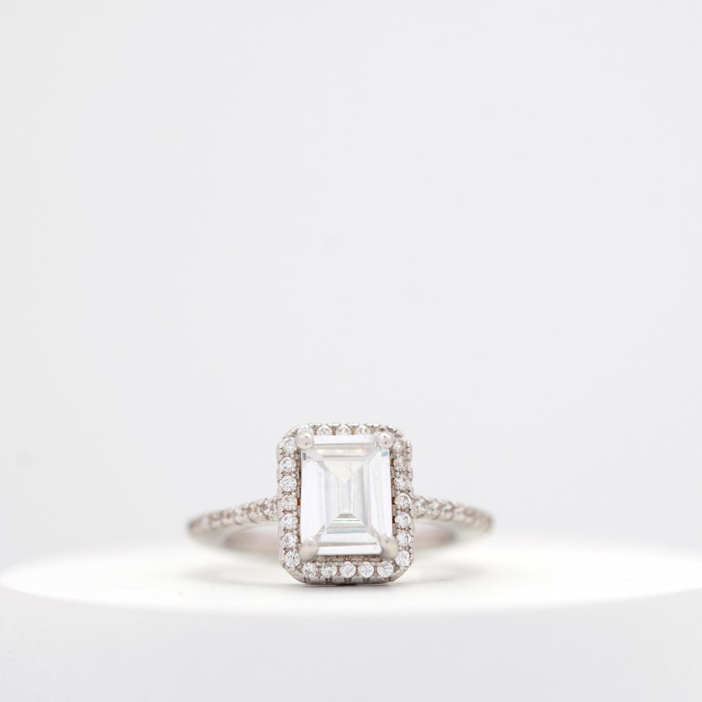 Elegant emerald-cut diamond engagement ring with a halo setting and a diamond-studded band displayed on a white background.