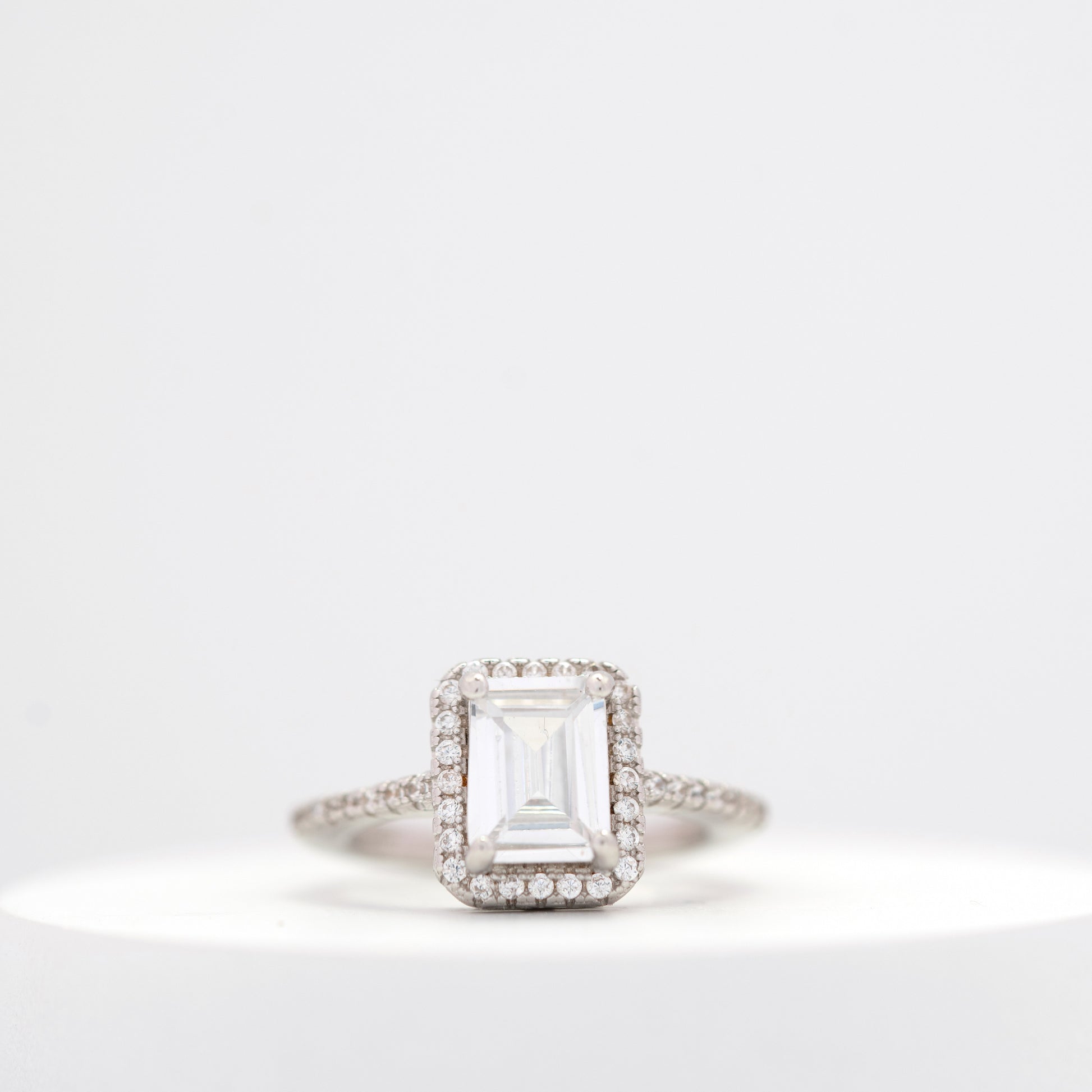 Elegant emerald-cut diamond engagement ring with a halo setting and a diamond-studded band displayed on a white background.