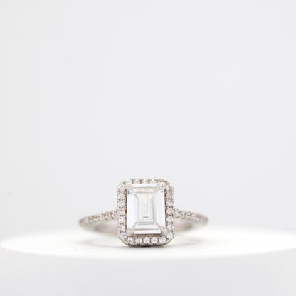 Elegant emerald-cut diamond engagement ring with a halo setting and a diamond-studded band displayed on a white background.
