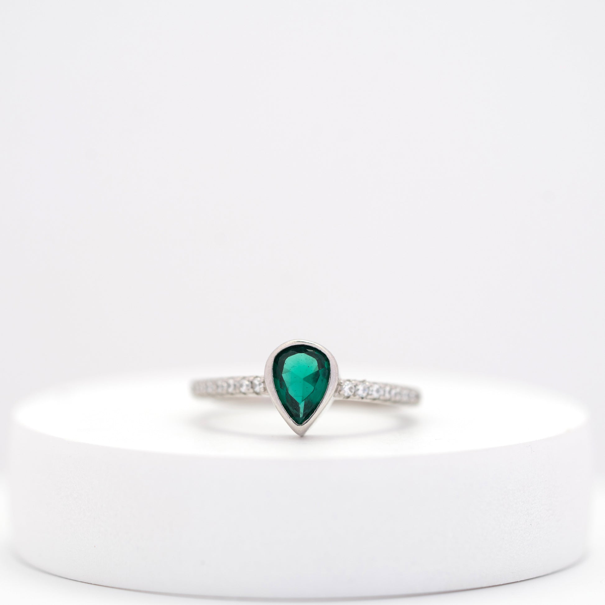 front view of elegant silver ring with teardrop emerald center stone and side diamonds