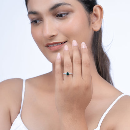 Elegant silver ring with teardrop emerald center stone and side diamonds on a model's hand
