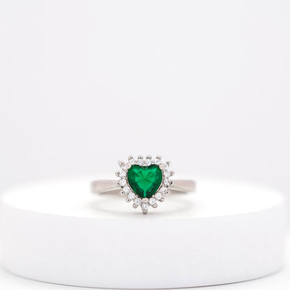 front view of heart emerald silver ring  surrounded by diamond clusters placed on a white stand