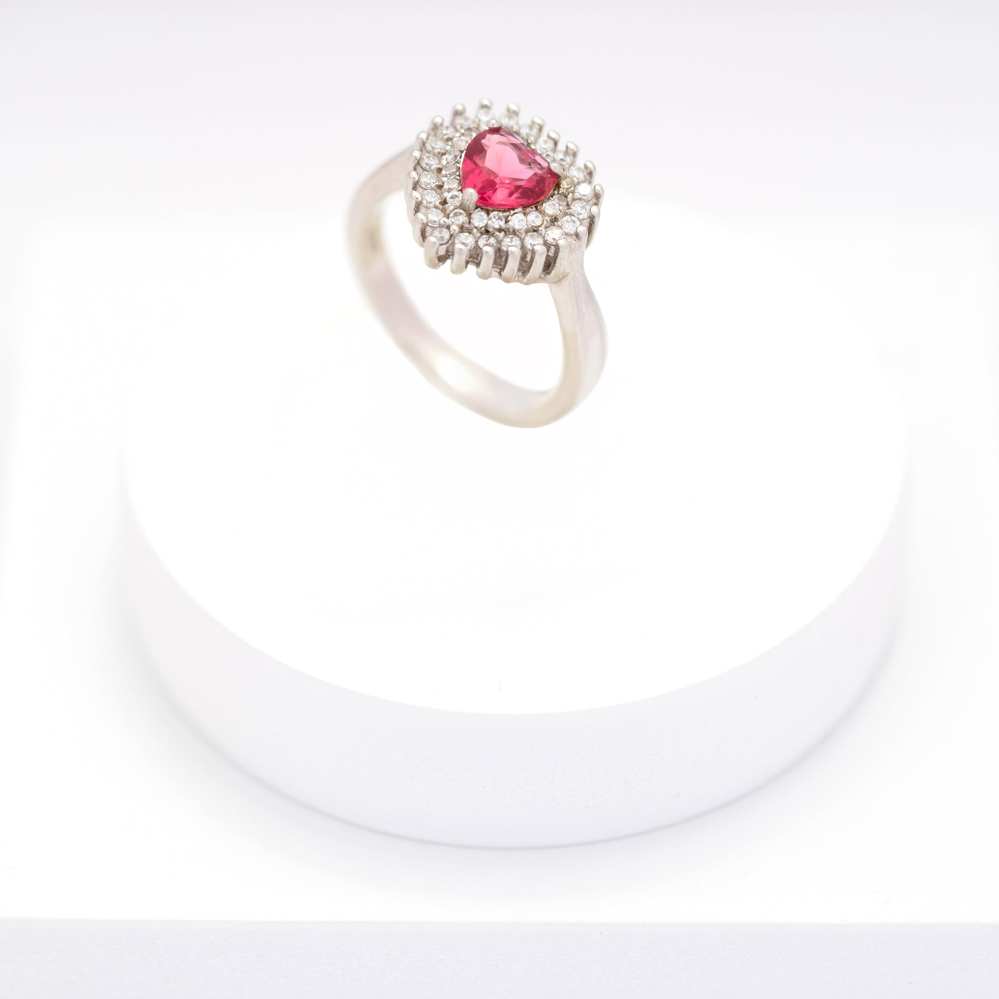 Silver ring with heart-shaped pink sapphire and diamond halo on a white stand