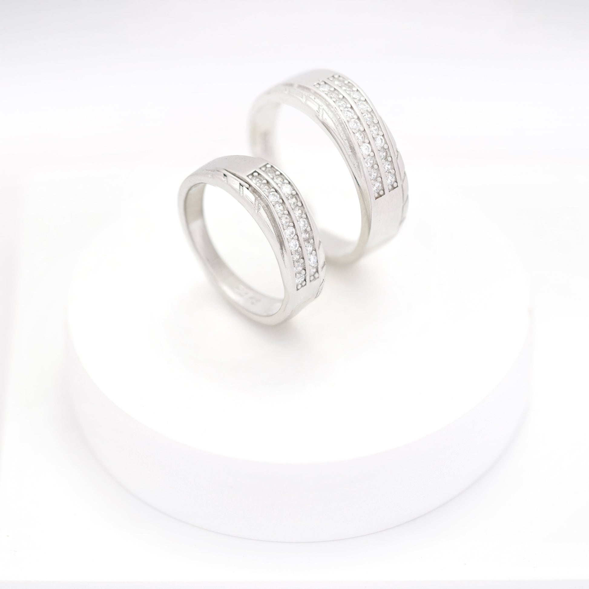 Matching silver couple bands with embedded diamonds displayed on a white round stand