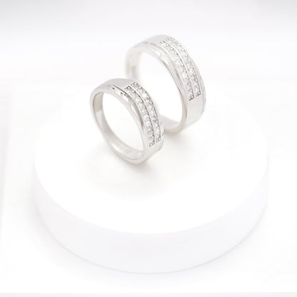 Matching silver couple bands with embedded diamonds displayed on a white round stand