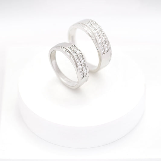 Matching silver couple bands with embedded diamonds displayed on a white round stand